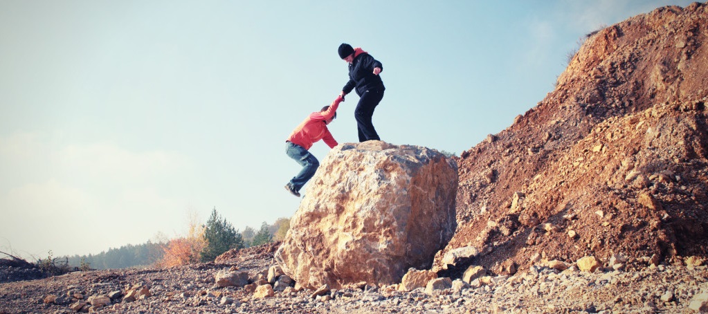 Photo of a person giving another person a helping hand climbing a rock
