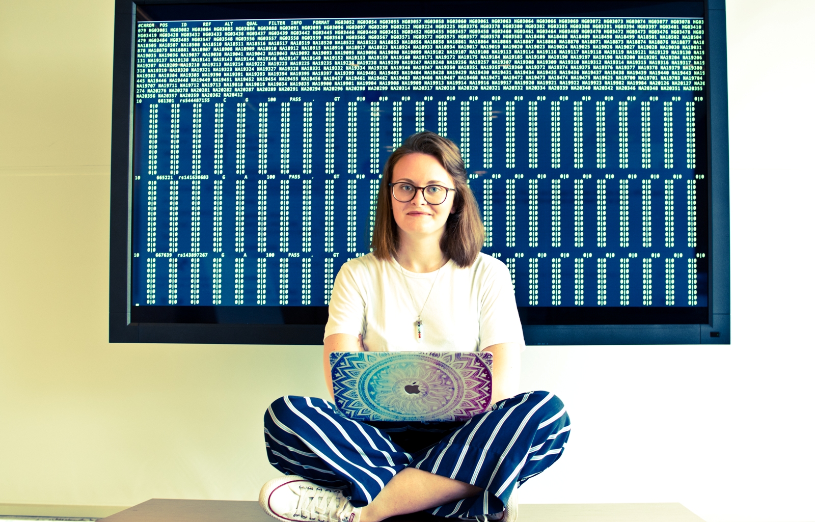 Emma Bailey sat with laptop and code on a screen behind