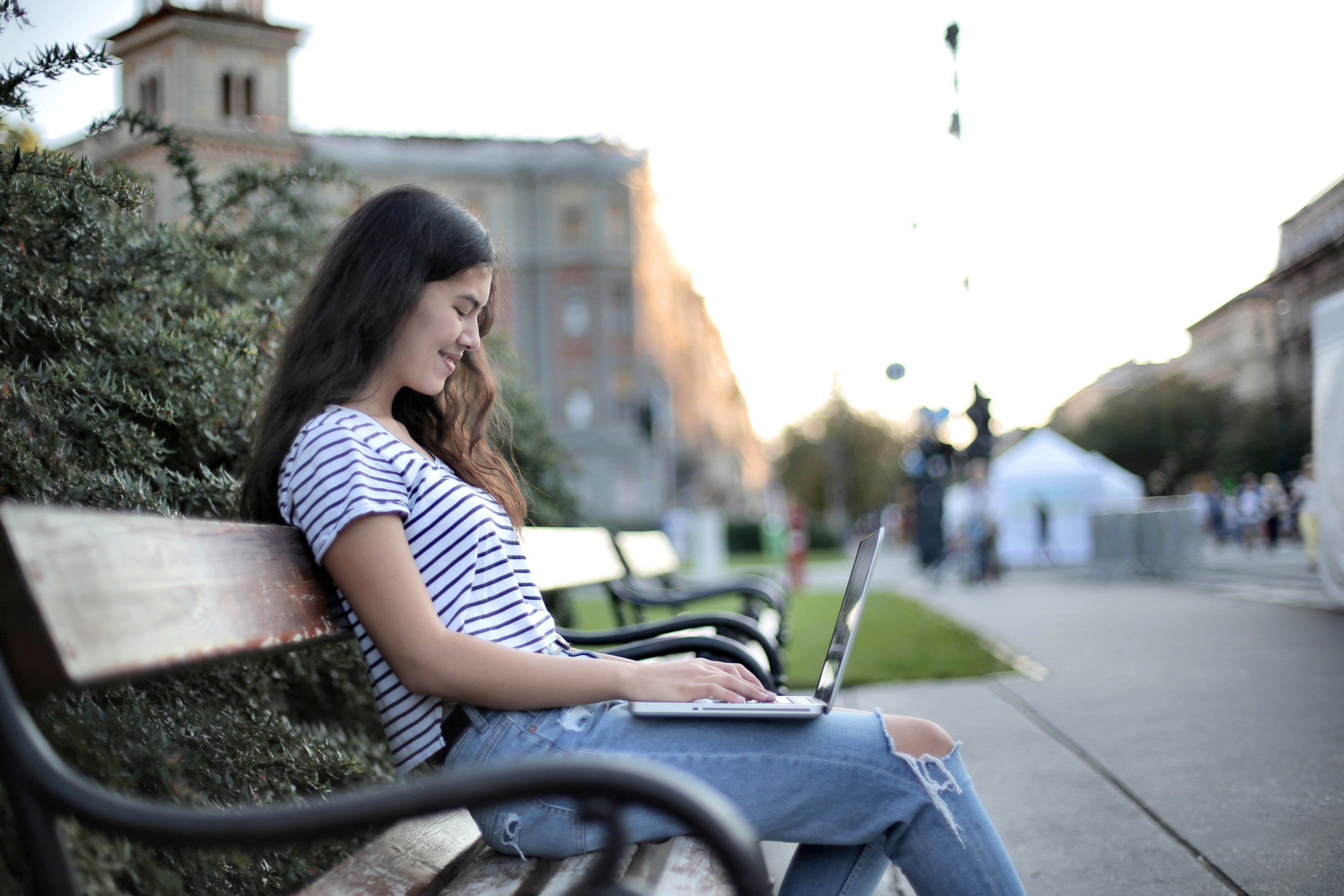 Young woman working on laptop sitting on a park bench.